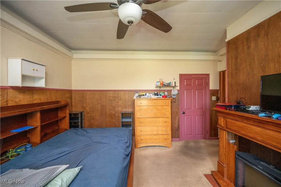 Carpeted bedroom with wooden walls, wainscoting, and ceiling fan