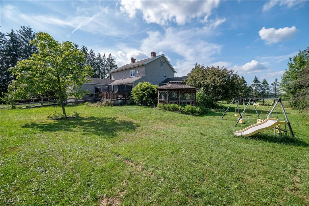View of green lawn with a gazebo, a playground, and view of wooded area