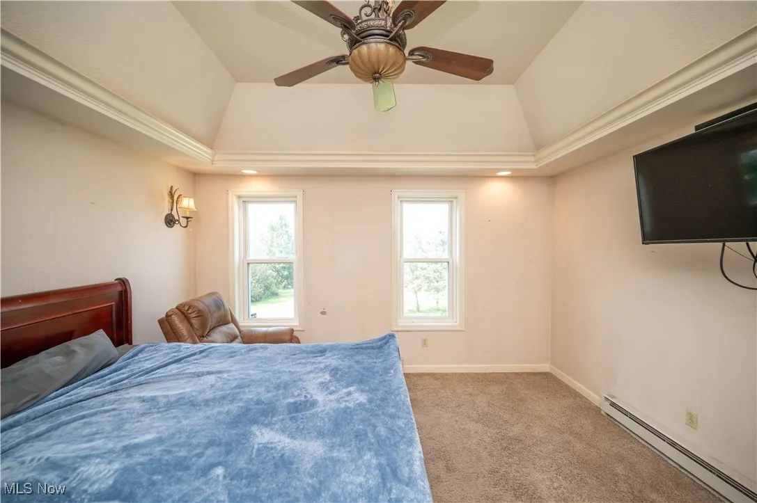 Carpeted bedroom with a baseboard radiator, a raised ceiling, and ceiling fan