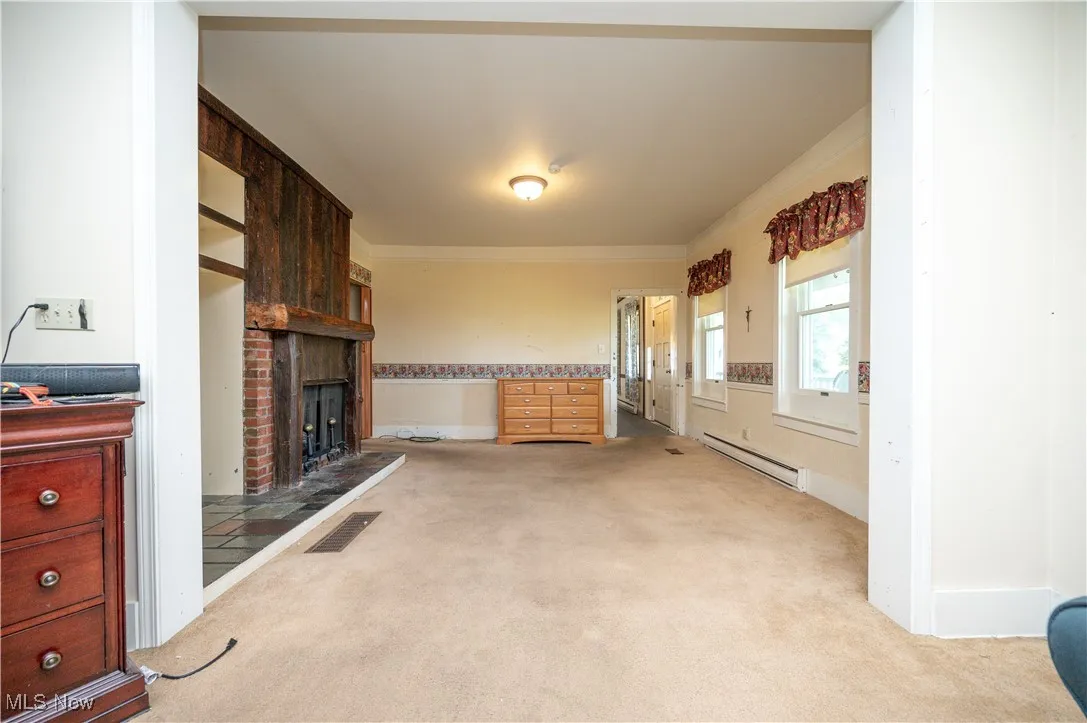 Unfurnished living room with a baseboard radiator, light colored carpet, a fireplace, and crown molding