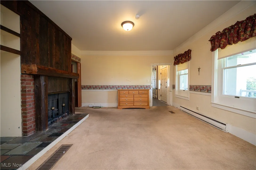 Unfurnished living room with a baseboard heating unit, carpet flooring, and a brick fireplace