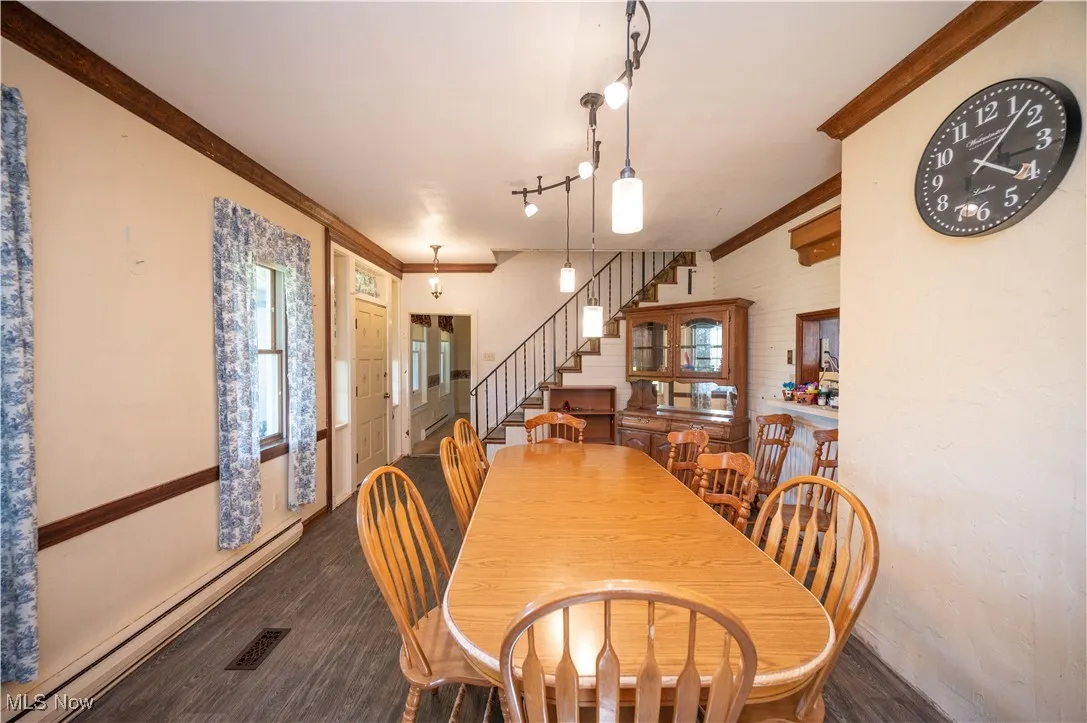 Dining room with a baseboard radiator, stairway, ornamental molding, and dark wood-type flooring