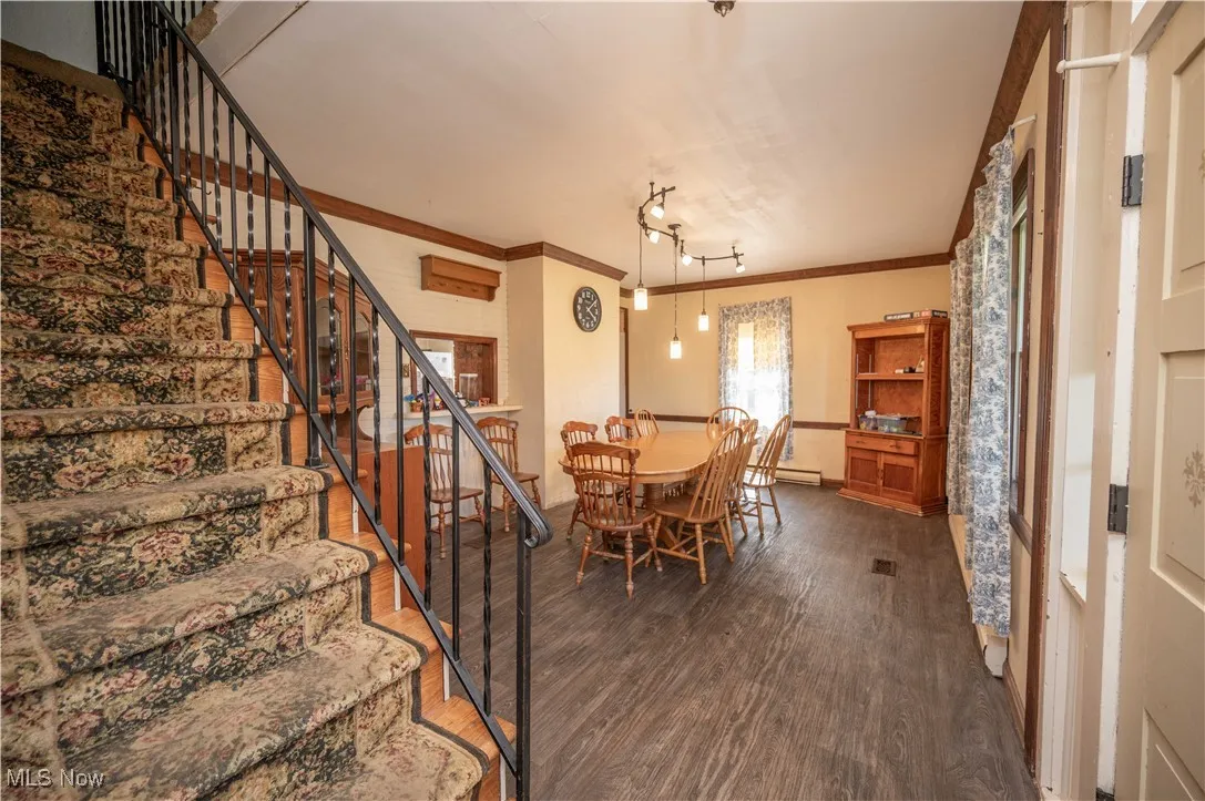 Dining room featuring dark wood finished floors, crown molding, and stairs
