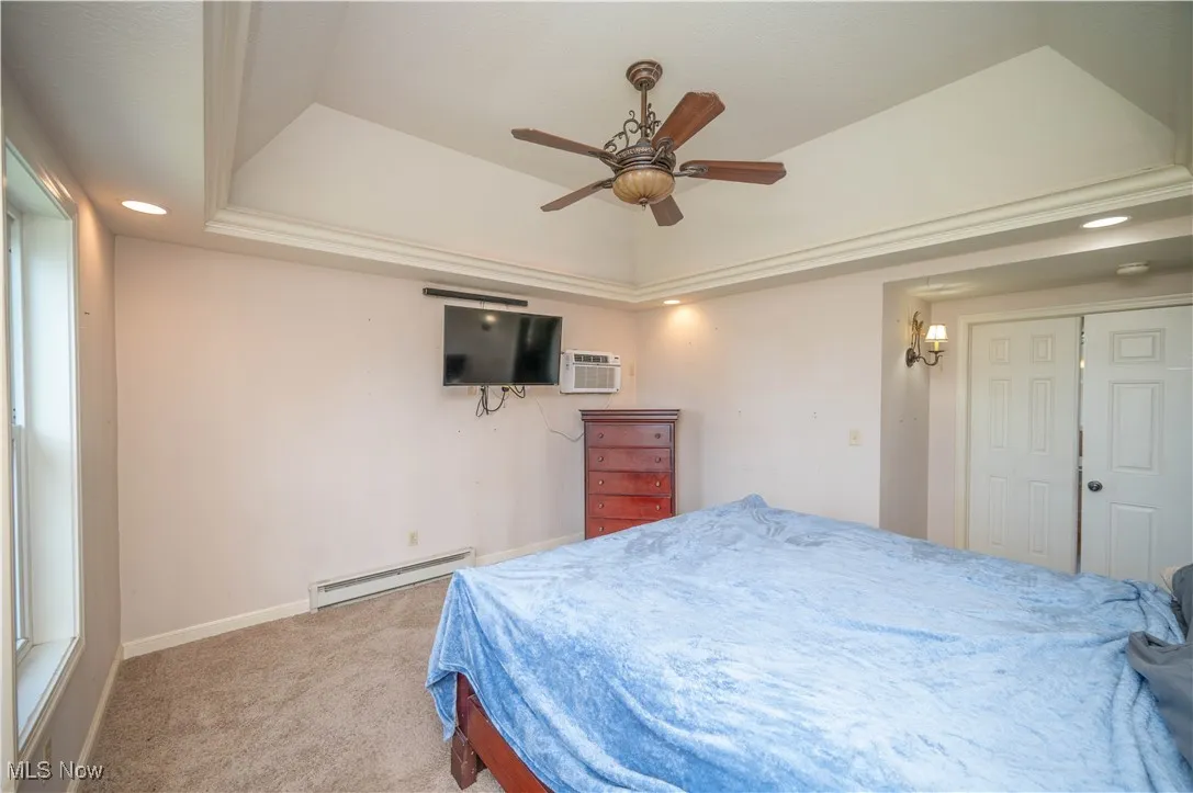 Bedroom with recessed lighting, a raised ceiling, carpet flooring, a baseboard radiator, and a wall mounted AC