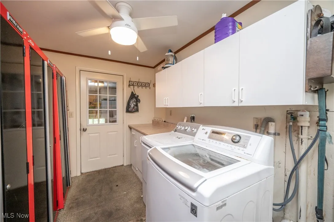 Washroom featuring cabinet space, washing machine and dryer, ornamental molding, light carpet, and ceiling fan