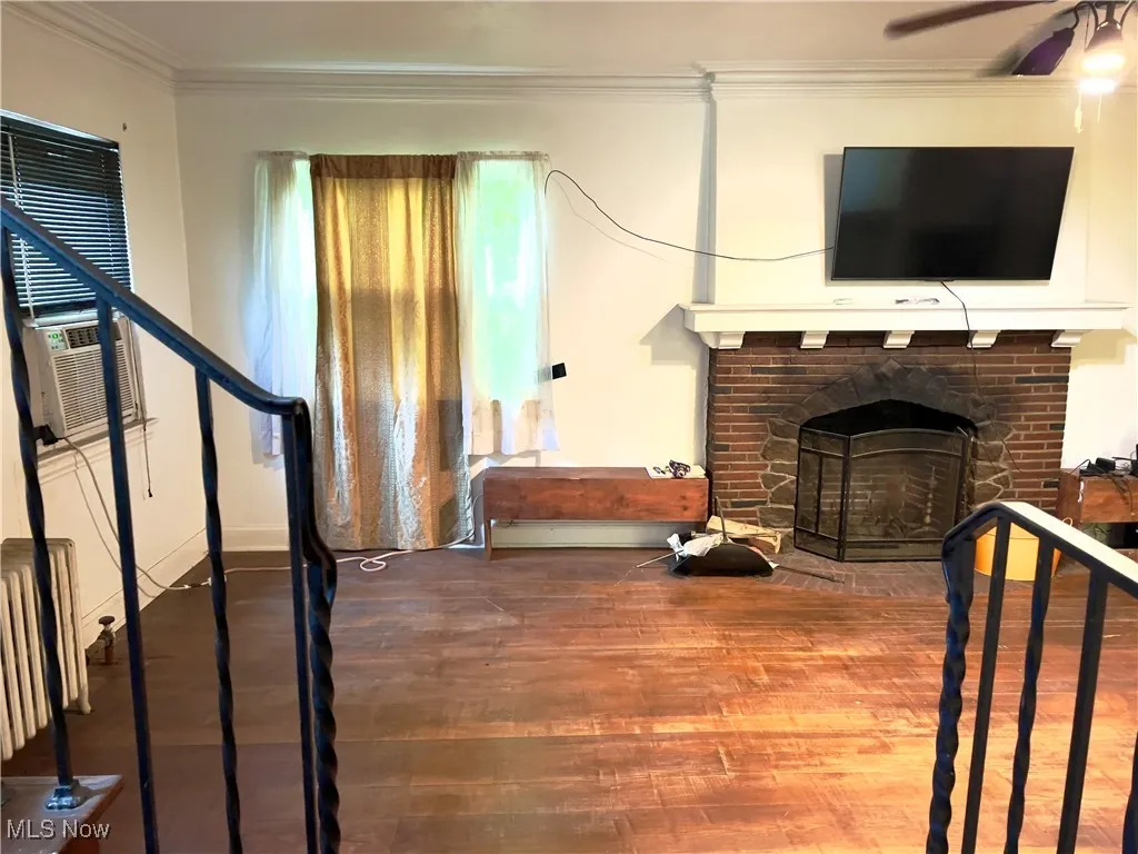 Living room featuring crown molding, wood finished floors, stairway, a brick fireplace, and radiator