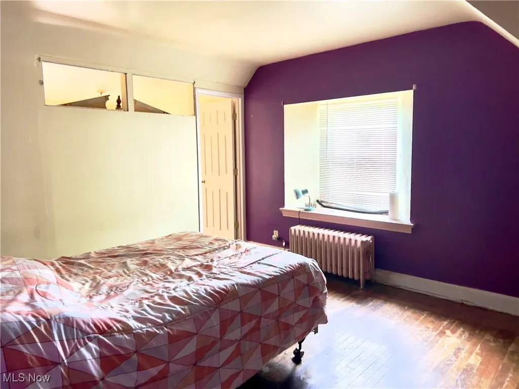 Master Bedroom featuring radiator heating unit, vaulted ceiling, and wood finished floors