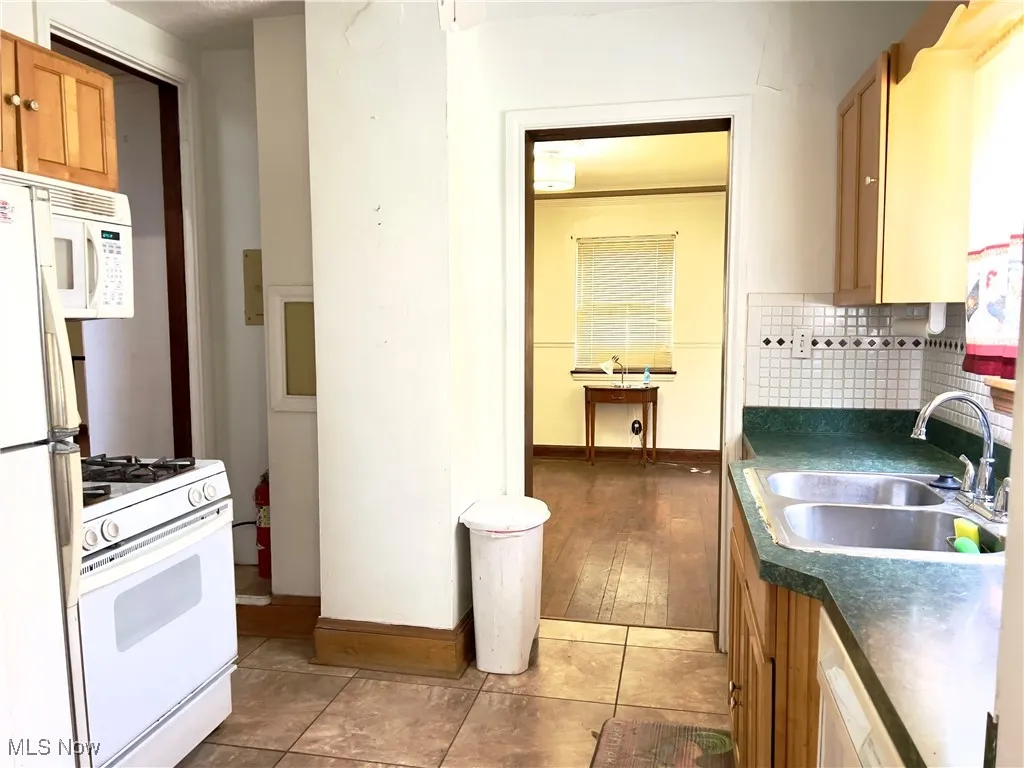 Kitchen with white appliances, dark countertops, tasteful backsplash, brown cabinets, and light tile patterned floors