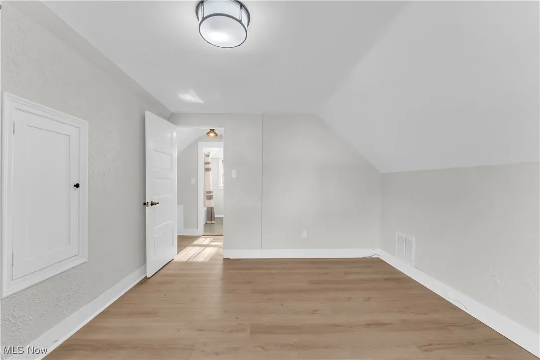 Bonus room featuring light wood-style flooring, a textured wall, and lofted ceiling