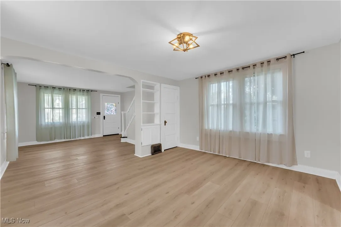 Unfurnished living room with stairway, light wood-type flooring, and arched walkways