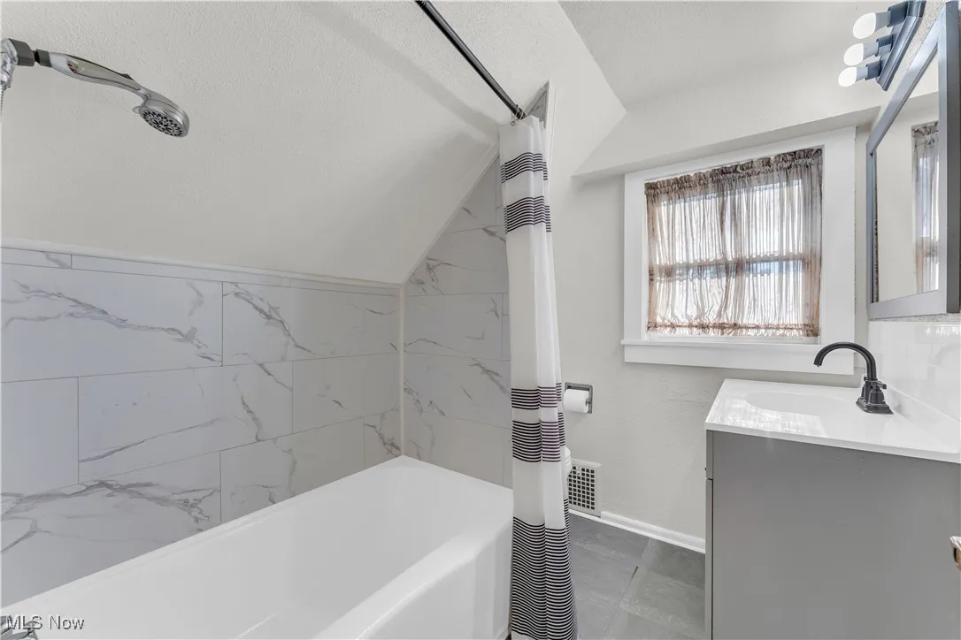 Bathroom with vanity, a textured ceiling, lofted ceiling, and shower / bath combo with shower curtain