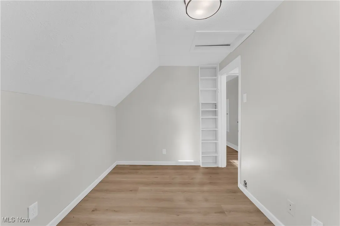 Additional living space featuring attic access, a textured ceiling, light wood-style flooring, and vaulted ceiling