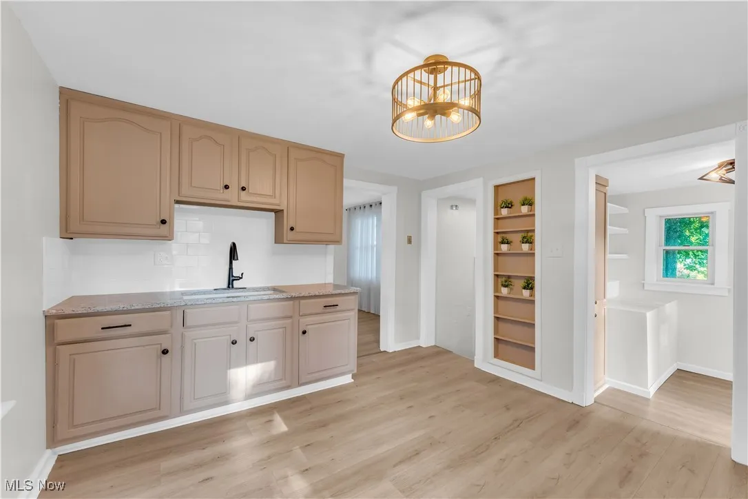 Kitchen with light wood-style floors, built in features, a chandelier, and light stone countertops
