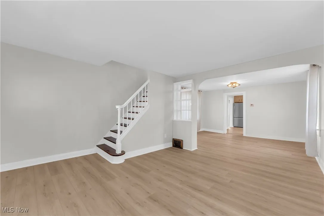 Unfurnished living room with light wood finished floors, stairway, and arched walkways