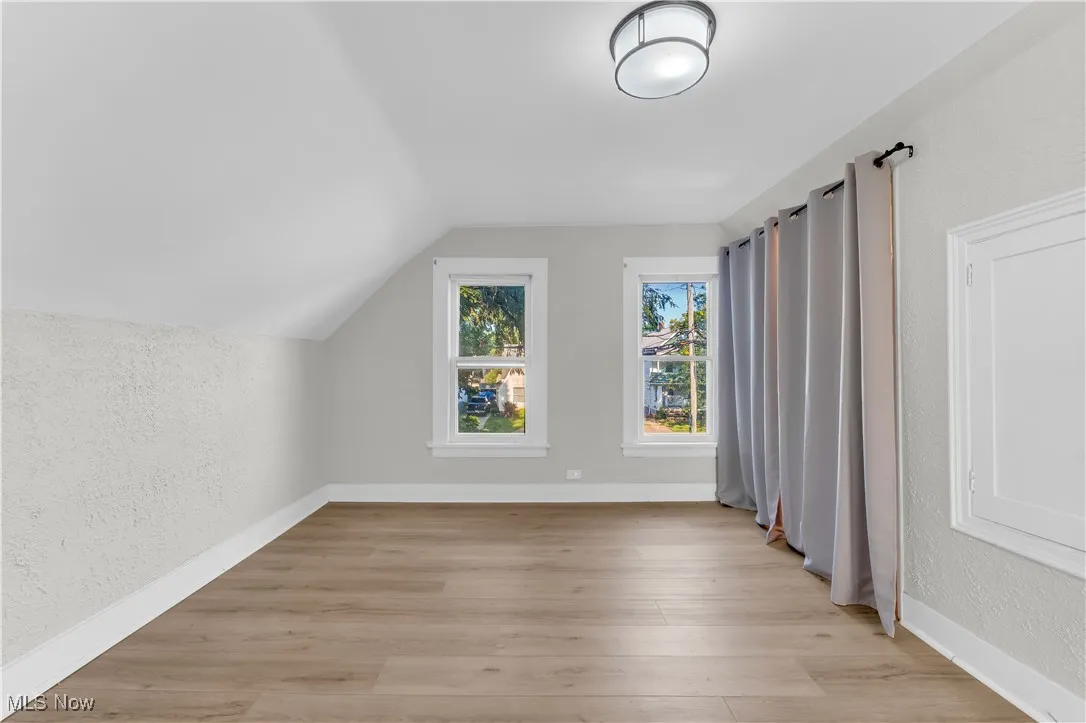 Additional living space with a textured wall, vaulted ceiling, and light wood-type flooring