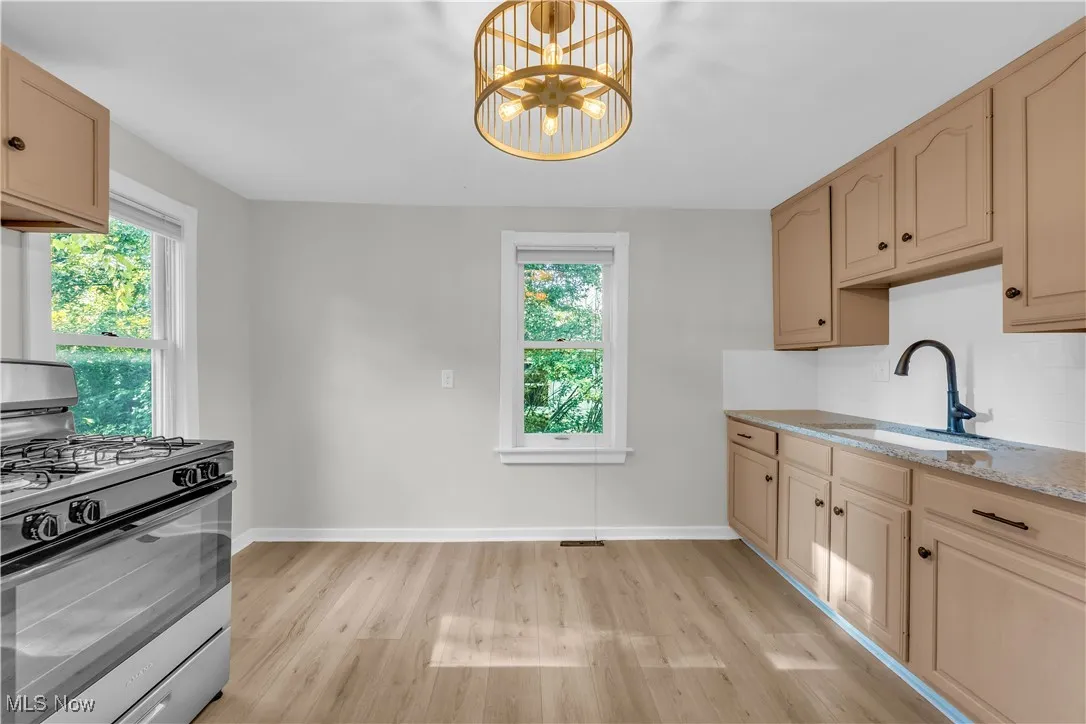 Kitchen featuring stainless steel range with gas cooktop, light wood-style floors, a chandelier, light stone countertops, and decorative light fixtures