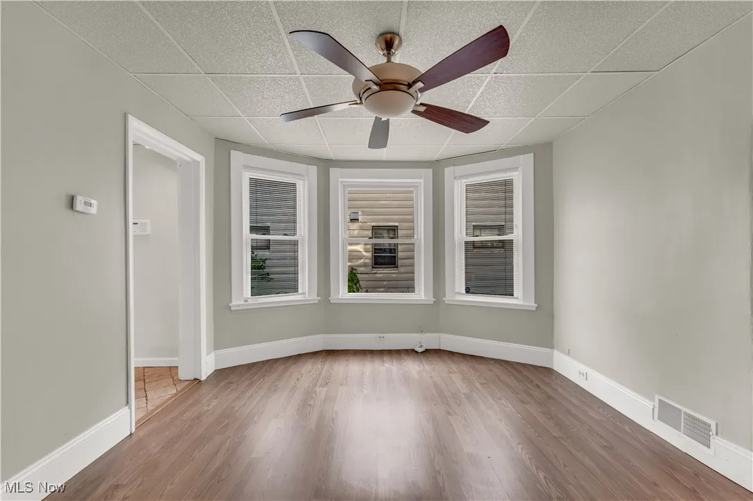 Empty room with a ceiling fan, wood finished floors, and a drop ceiling