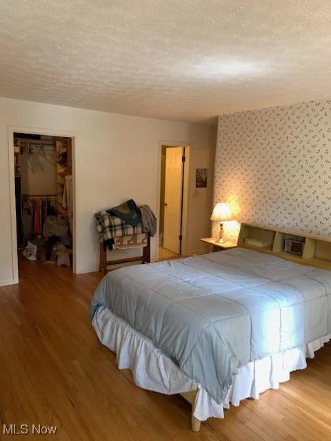 Bedroom featuring a textured ceiling, wood finished floors, and a walk in closet