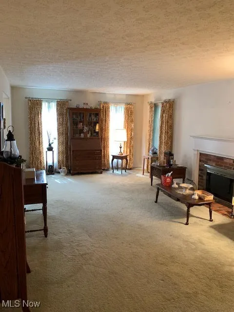 Living area featuring carpet, a brick fireplace, and a textured ceiling
