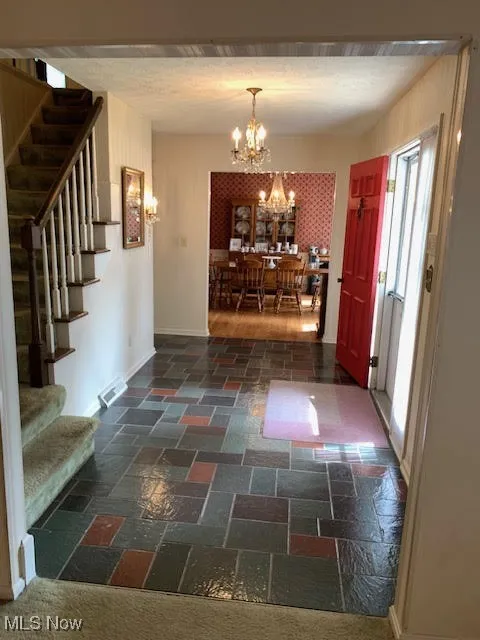 Foyer featuring stairway, a chandelier, and stone tile floors