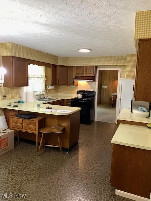 Kitchen featuring light countertops, a peninsula, black range, a textured ceiling, and a breakfast bar area