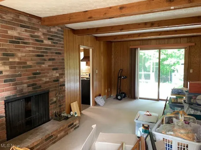 Carpeted living room with wooden walls, a fireplace, and beam ceiling