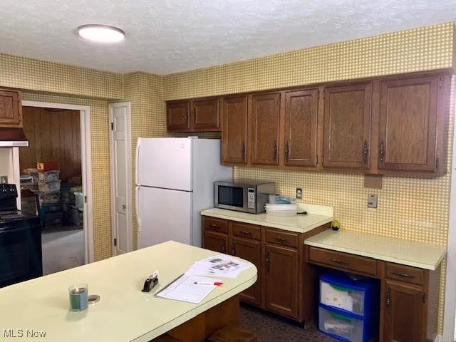 Kitchen featuring light countertops, black range, wallpapered walls, a textured ceiling, and stainless steel microwave