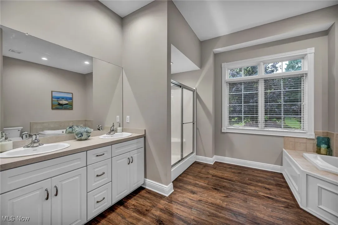 Full bath with a garden tub, wood finished floors, a stall shower, and double vanity