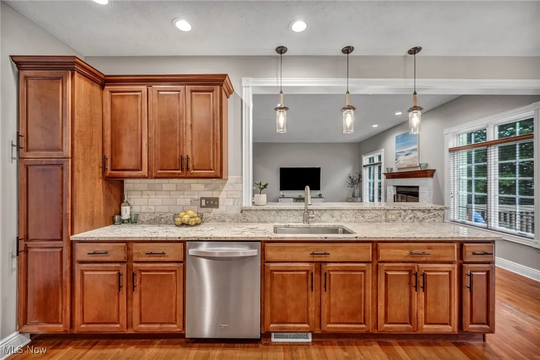 Kitchen featuring dishwasher, wood finished floors, brown cabinets, a fireplace, and light stone countertops