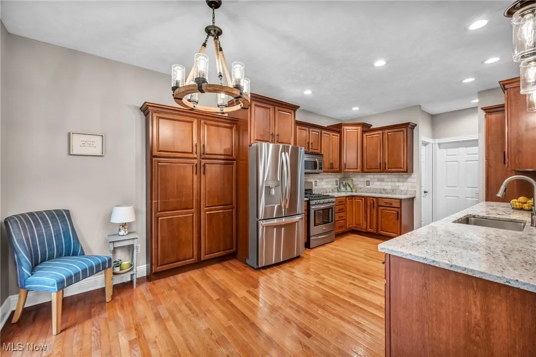 Kitchen featuring stainless steel appliances, brown cabinets, light wood-style flooring, decorative backsplash, and light stone countertops