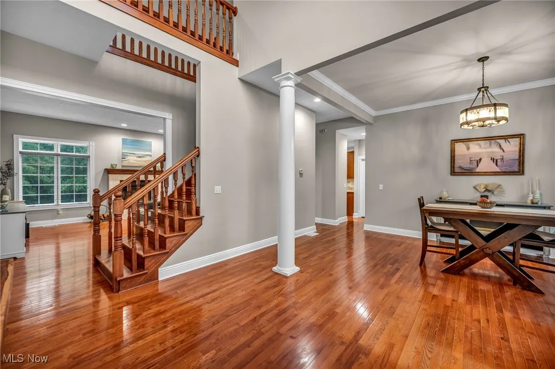 Dining room with ornate columns, hardwood / wood-style floors, crown molding, stairway, and a chandelier