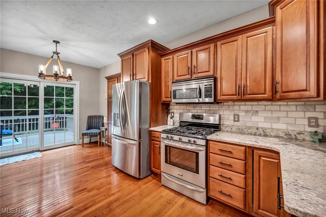Kitchen featuring stainless steel appliances, brown cabinetry, light wood-style floors, tasteful backsplash, and a textured ceiling
