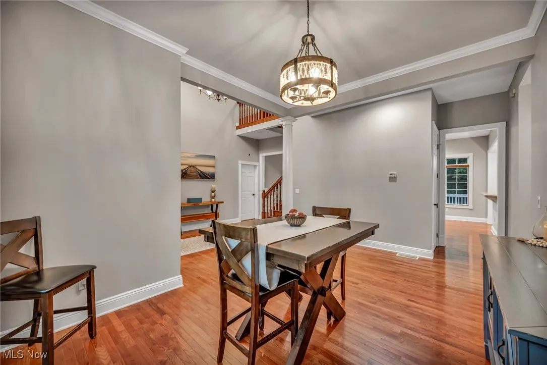 Dining space with a chandelier, ornate columns, light wood-style floors, stairway, and crown molding