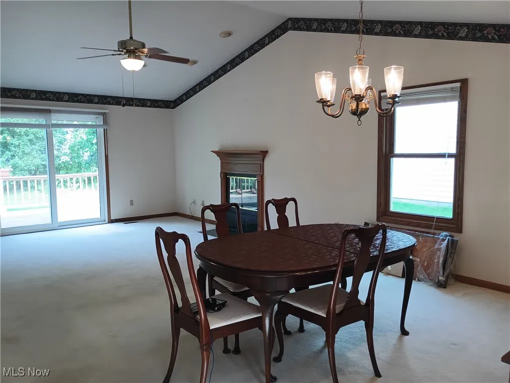 Dining room with light carpet, vaulted ceiling, ceiling fan, a chandelier, and a high end fireplace