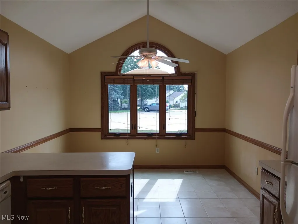 Kitchen featuring light countertops, white appliances, vaulted ceiling, light tile patterned flooring, and a peninsula