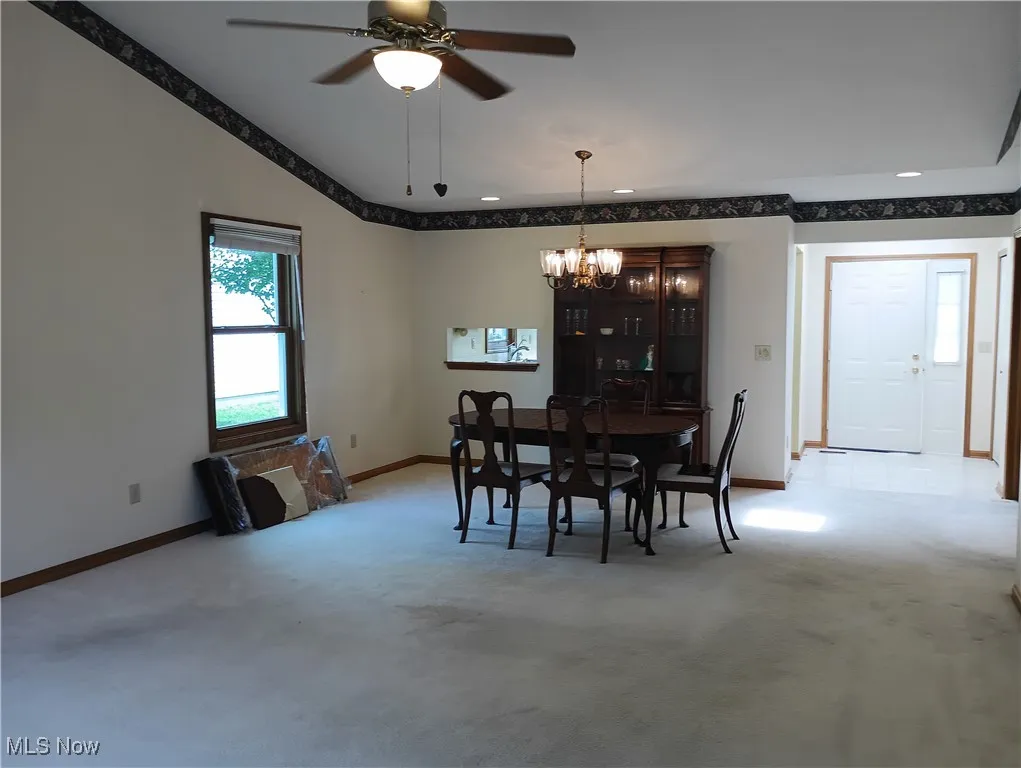 Dining space with light colored carpet, a chandelier, a ceiling fan, and lofted ceiling