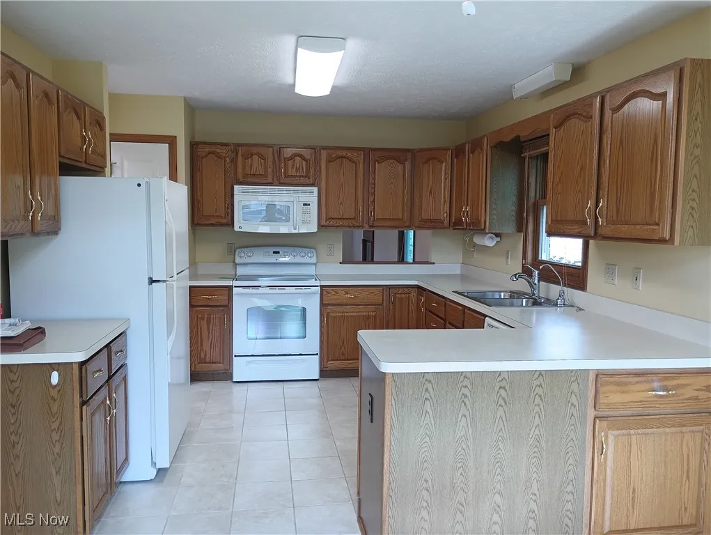 Kitchen featuring white appliances, a peninsula, light countertops, and brown cabinetry