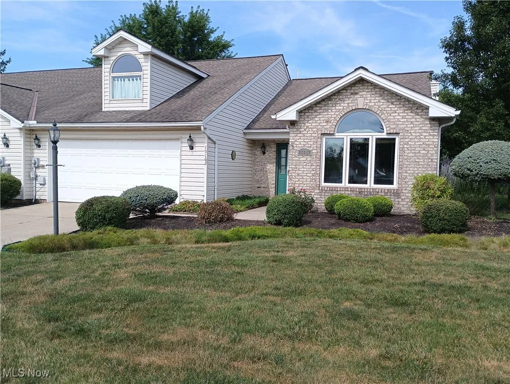 View of front facade featuring roof with shingles, a garage, a front lawn, driveway, and brick siding