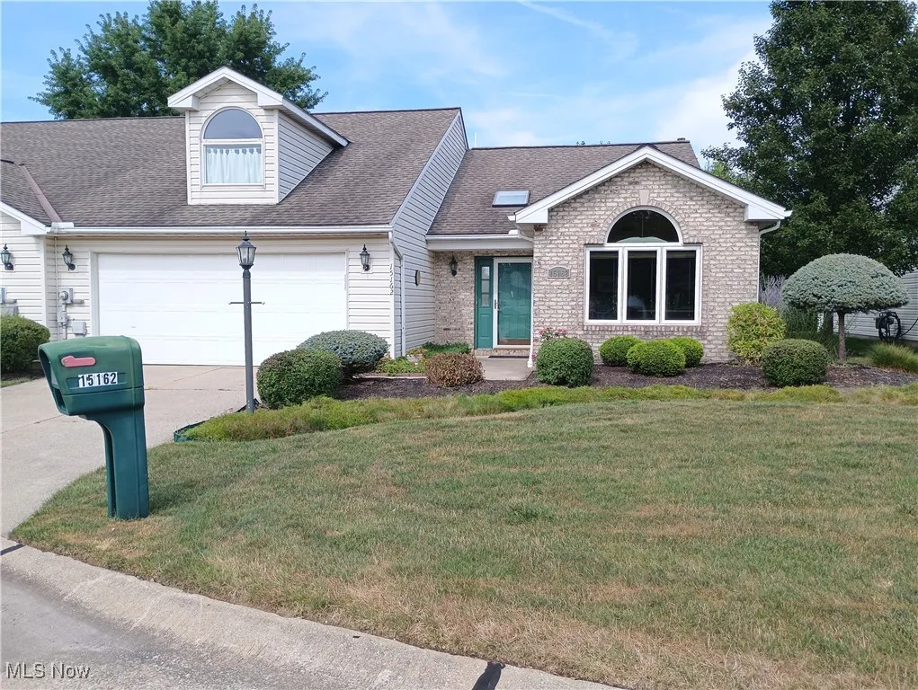 View of front of house with a shingled roof, a front lawn, driveway, an attached garage, and brick siding