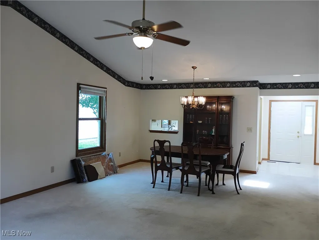 Dining area with light carpet, a chandelier, lofted ceiling, and a ceiling fan