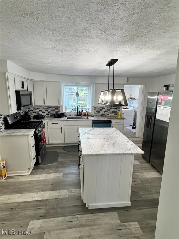 Kitchen featuring stainless steel appliances, a textured ceiling, a kitchen island, white cabinets, and tasteful backsplash