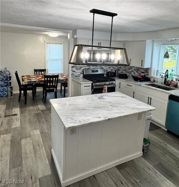 Kitchen with gas range, a textured ceiling, tasteful backsplash, a kitchen island, and white cabinetry