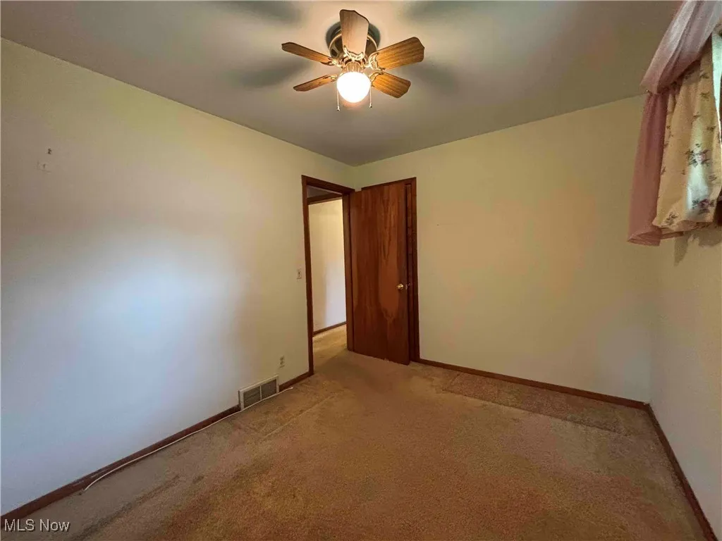 Empty room with light colored carpet and a ceiling fan