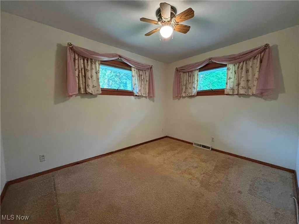 Carpeted empty room with baseboards and a ceiling fan
