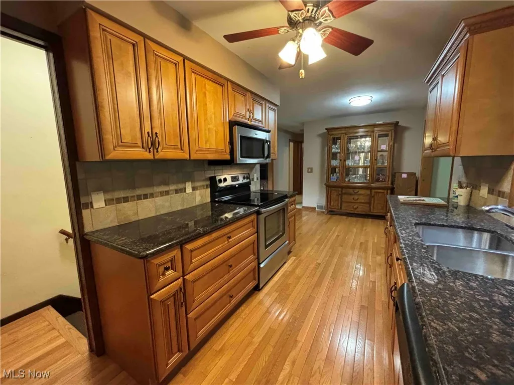 Kitchen with brown cabinetry, stainless steel appliances, light wood-style flooring, and decorative backsplash