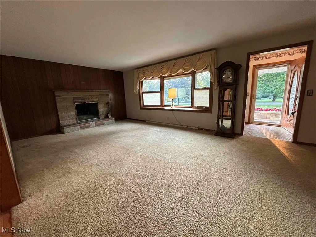 Unfurnished living room featuring a stone fireplace, wood walls, and light colored carpet