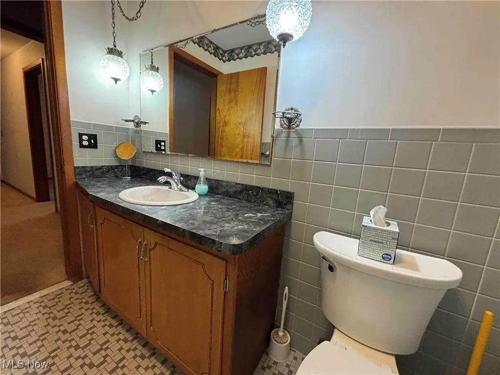 Half bathroom featuring vanity, tile walls, and a wainscoted wall