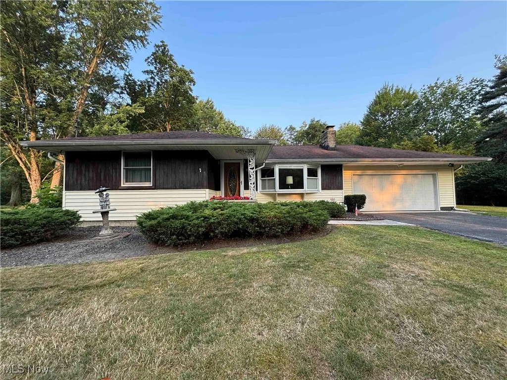 View of front of house with a garage, asphalt driveway, a chimney, and a front lawn