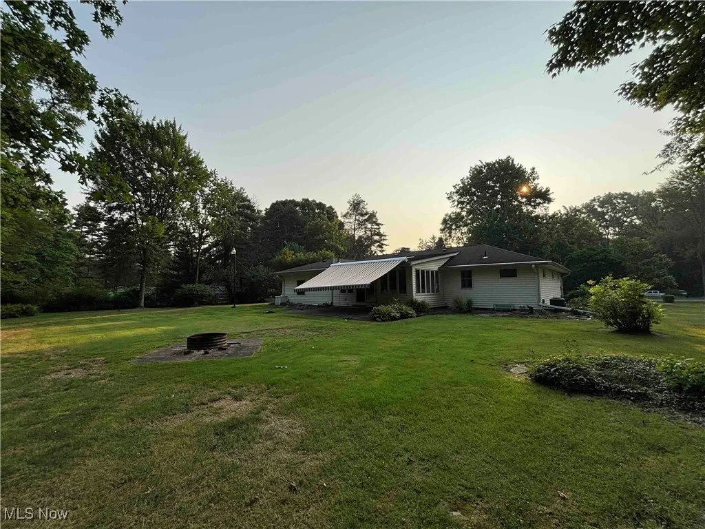 Yard at dusk featuring a fire pit, a lawn, and view of scattered trees