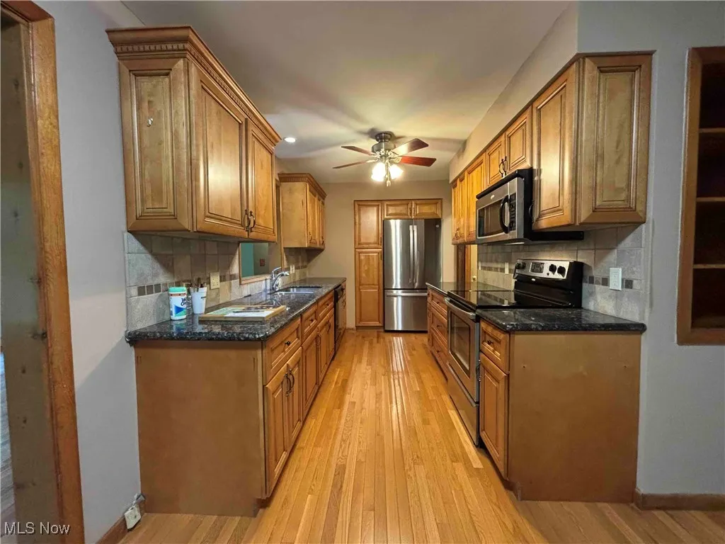 Kitchen with appliances with stainless steel finishes, light wood-style floors, decorative backsplash, and brown cabinetry